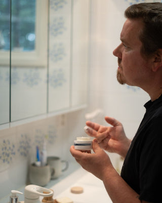 24H Kasvovoide herkälle iholle, pitkäkestoinen kosteutus, tukee ihon suojamuuria, rauhoittaa, hajusteeton, UNISEX, mies levittää voidetta kasvoille.